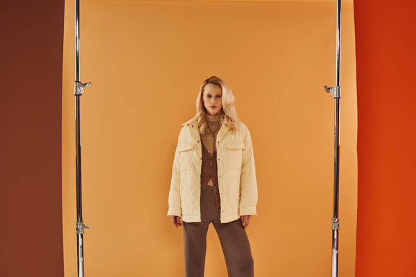 привлекательная женщина в осеннем наряде смотрит в камеру и позирует на бежевом фоне, уютные слои