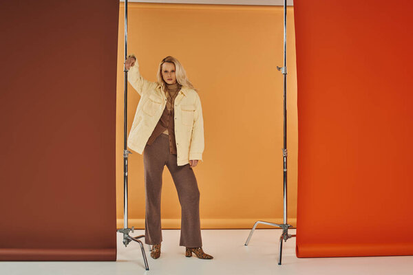 красивая блондинка в осеннем наряде смотрит в камеру и позирует на пастельном фоне, верхняя одежда