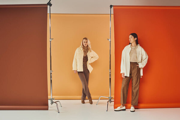 autumn fashion, young interracial women in stylish attire posing on pastel multicolored backdrop