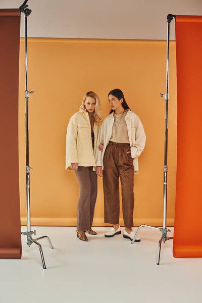 fall fashion, young and stylish women in autumn attire posing on pastel multicolored backdrop