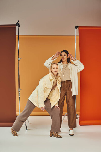 fall fashion, young and stylish women in autumn clothes posing on multicolored backdrop, diversity
