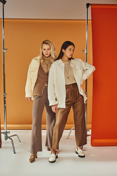 осенняя мода, молодые межрасовые модели в осеннем наряде и туфли позируют на красочном пастельном фоне