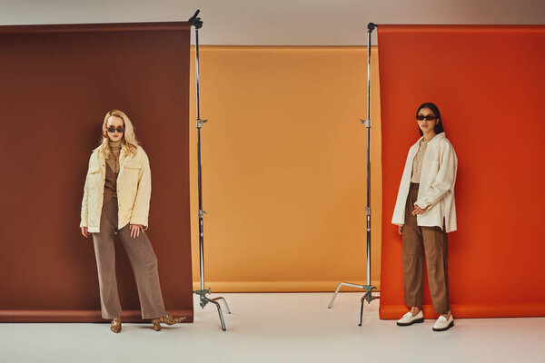 Осенняя мода, стильные мультиэтнические модели в солнцезащитных очках и верхней одежде позируют на красочном фоне