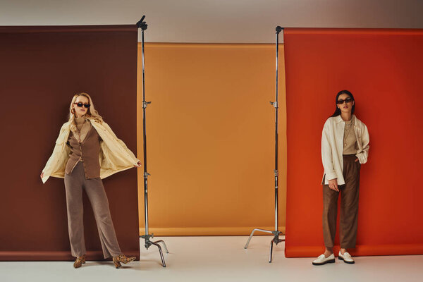 Осенний гардероб, стильные мультиэтнические модели в солнцезащитных очках и верхней одежде позируют на красочном фоне