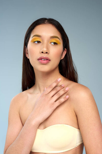 young asian model with bold makeup posing in strapless top isolated on blue, diverse beauty concept