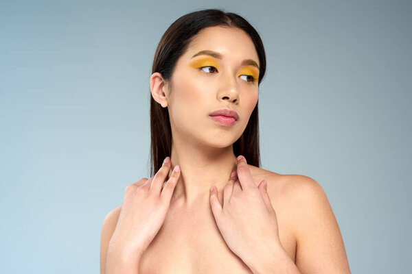 pretty model with bold makeup and bare shoulders posing on blue backdrop, asian beauty concept