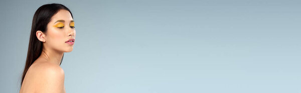 beauty, asian model with bold makeup and bare shoulders posing on blue backdrop, elegance, banner