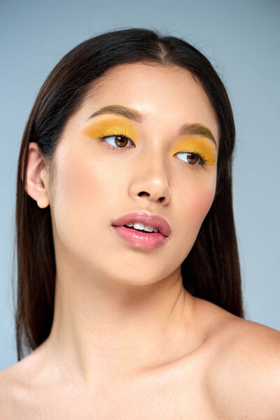 женская элегантность, красивая азиатка с смелым макияжем и обнаженными плечами, позирующая на голубом фоне