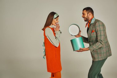 Modayı takip eden adam turuncu elbiseli kadının hediye kutusunu açıyor. Gri, retro-ilham verici çifte.