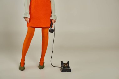 Kırpılmış turuncu elbiseli kadın manzarası ve gri, eski moda telefon ahizeli tayt.