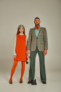 Moda modası geçmiş eski moda elbiseli genç bir çift. Gri renkli cep telefonlarıyla duruyorlar.