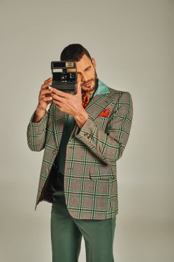 Kareli ceketli şık bir adam gri, eski moda bir kamerayla fotoğraf çekiyor.