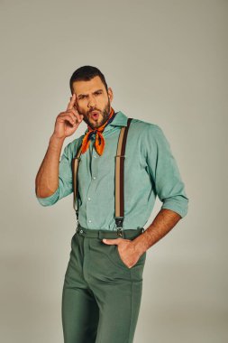 Eski giysiler içinde hayrete düşmüş bir adamın gri renkte el ele tutuşup alnına dokunması.