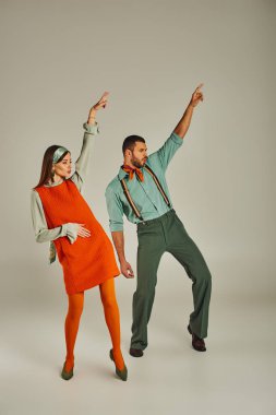 stylish couple in vintage clothes dancing with raised hands on grey, retro vibes and excitement clipart