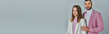 Beyaz takım elbiseli zarif bir kadının yanında leylak rengi ceketli, kendine güvenen bir adam. Gri, iş modasında, pankartta.