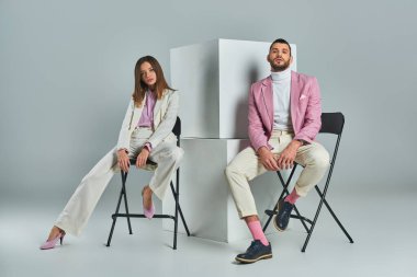 Şık giyinen kendine güvenen çift gri, minimalist moda küplerinin yanındaki sandalyelerde otururlar.