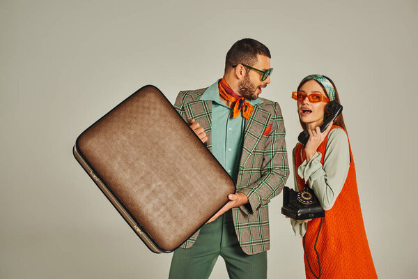 excited man with vintage suitcase near retro style woman talking on corded phone on grey