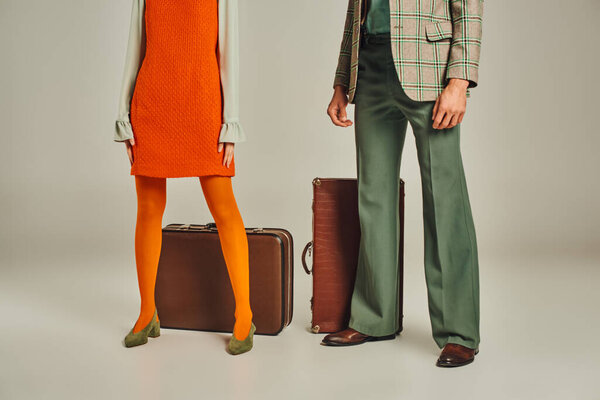 cropped view of retro travelers in orange dress and plaid blazer near vintage suitcases on grey