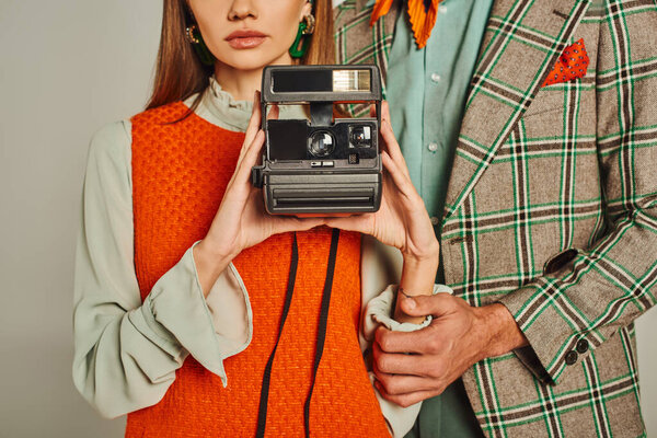 cropped view of woman in orange dress holding vintage camera near man in plaid jacket on grey
