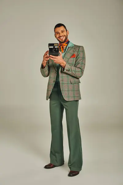グレーの背景にヴィンテージカメラで立っているスタイリッシュなレトロな服装の楽しい男の完全な長さ — ストック写真