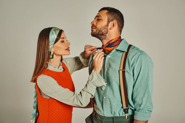 очаровательная женщина привязывает яркий шейный платок к стильному мужчине в подтяжках на серой, винтажной моде