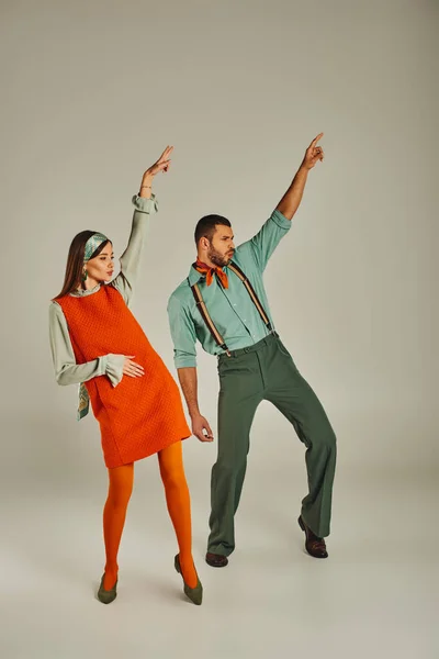 stylish couple in vintage clothes dancing with raised hands on grey, retro vibes and excitement