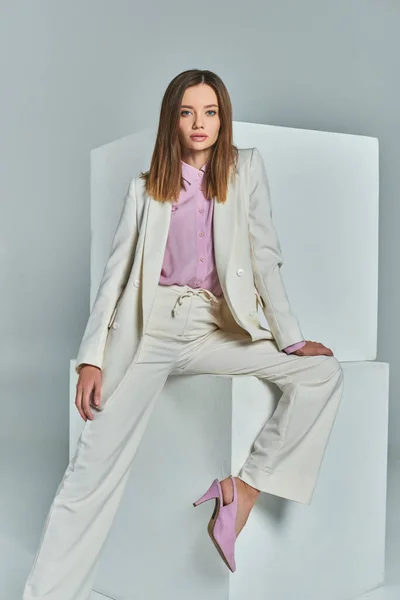 stock image attractive woman in elegant suit posing near white cubes on grey, minimalistic business fashion