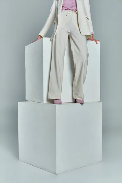 灰色の背景に白い立方体の上に立っているエレガントなフォーマルな服装の若い女性の見た目 — ストック写真