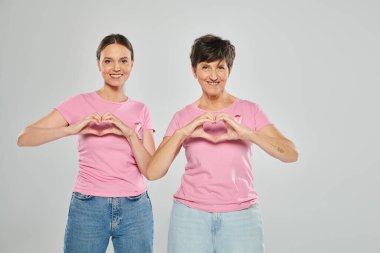 Göğüs kanseri konsepti, mutlu kadınların kameraya bakması ve elleri gri arkaplanda kalbini göstermesi.