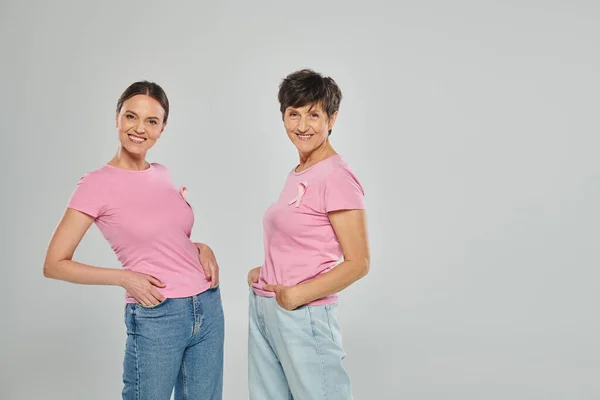 stock image breast cancer concept, support campaign, two women looking at camera, smile, grey backdrop
