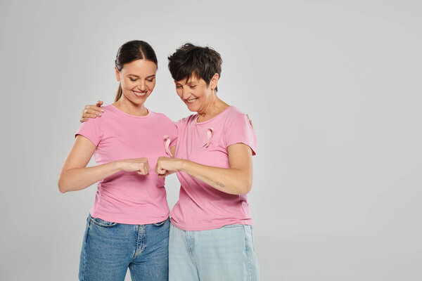 breast cancer concept, happy women with pink ribbons fist bumping on grey backdrop, cancer free