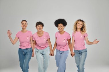Göğüs kanseri farkındalığı, pembe kurdeleli neşeli çok kültürlü kadınlar gri üzerinde birlikte yürüyorlar.