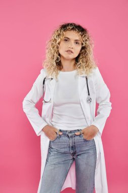 Göğüs kanseri farkındalığı, kameraya bakan kıvırcık kadın doktor, pembe fon, mutlu kadın.