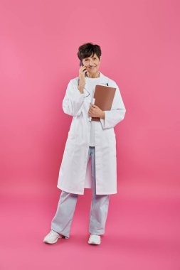 Kadın onkolog, elinde dosya olan olgun bir doktor akıllı telefonla konuşuyor, meme kanseri farkındalığı var.