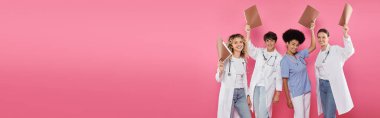 Sırıtkan çok ırklı doktorlar pembe, afiş ve meme kanseri aylarında izole edilmiş kağıt klasörler taşıyorlar.