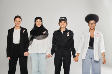 Gri, meme kanserine izole edilmiş pembe kurdeleli farklı ırklar arası kadınlar gülümsüyor.