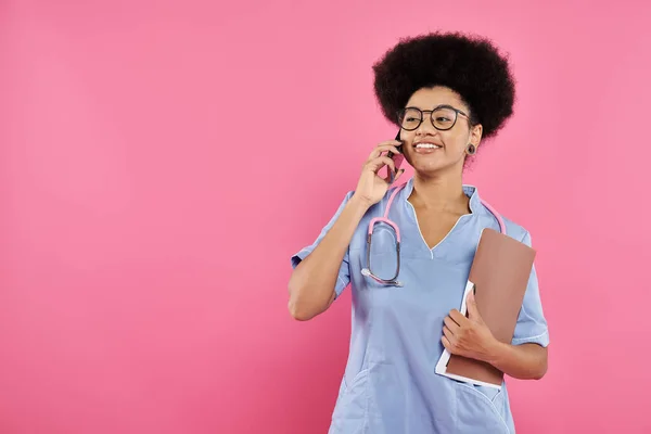 stock image breast cancer awareness, african american doctor, happy oncologist with folder talking on smartphone