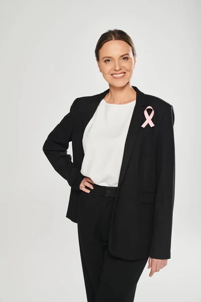 stock image smiling businesswoman with pink ribbon on jacket isolated on grey, breast cancer awareness