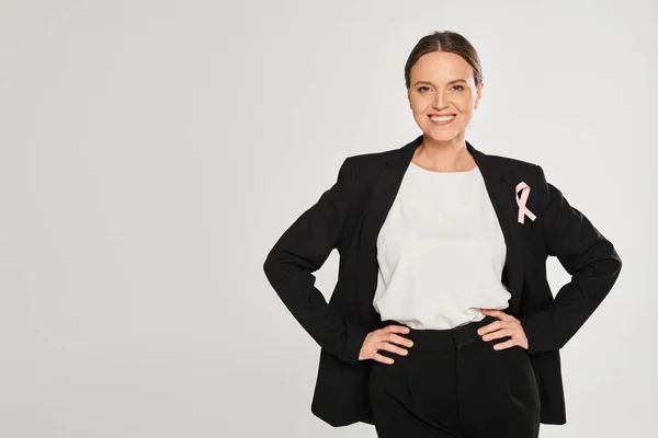 stock image smiling businesswoman with pink ribbon on jacket posing at camera isolated on grey, breast cancer