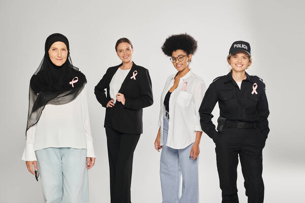 веселые различные многоэтнические женщины с розовыми лентами рака молочной железы, изолированные на сером