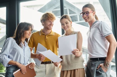 Şık günlük giysiler içinde neşeli iş arkadaşları cam zemin ile çalışma kağıtlarına bakıyor, birlikte çalışıyorlar.