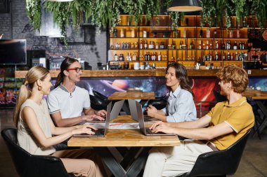 Hardworking cheerful team using laptops and smiling to each other with blurred backdrop, coworking stock vector