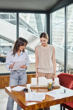 two team members focused on scale model and paperwork with glass on backdrop, design bureau clipart