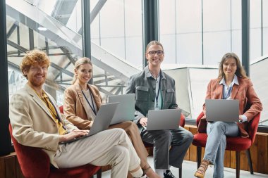 team of cheerful coworkers in smart casual wear holding laptops and looking at camera, coworking clipart