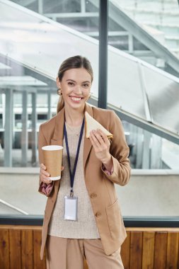 young woman in smart casual attire enjoying sandwich and coffee looking at camera, coworking concept clipart
