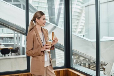 happy blonde woman enjoying her sandwich and coffee during lunch break at work, coworking concept clipart