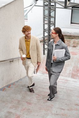 two young male colleagues walking upstairs talking and smiling at each other, coworking concept clipart
