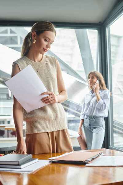 young colleagues working, looking at papers with one talking on phone on glass backdrop, coworking