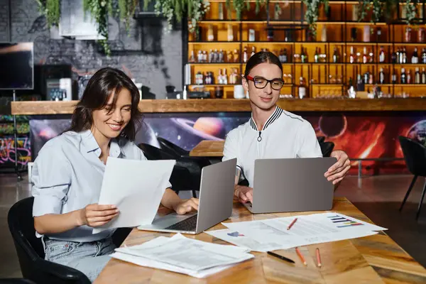 Stock image concentrated smiley colleagues working on documents using laptops with blurred backdrop, coworking