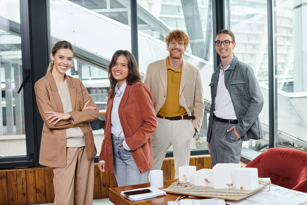 creative team in smart casual outfits posing near table with papers and scale model, design bureau